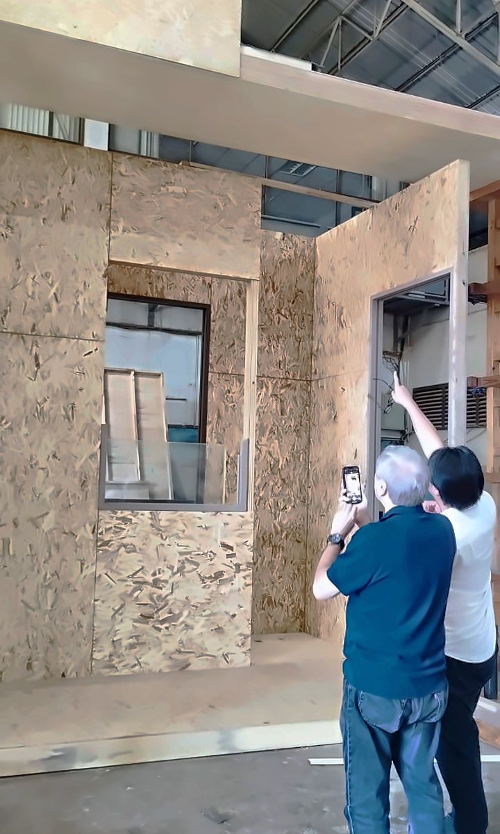 Two people inspecting a building module under construction, with OSB-lined walls on a timber floor